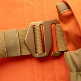 Close-up of a brown plastic buckle fastened to a tan strap on orange fabric, part of the Duck Camp Canvas Upland Strap Vest—durable hunting gear designed for upland pursuits.