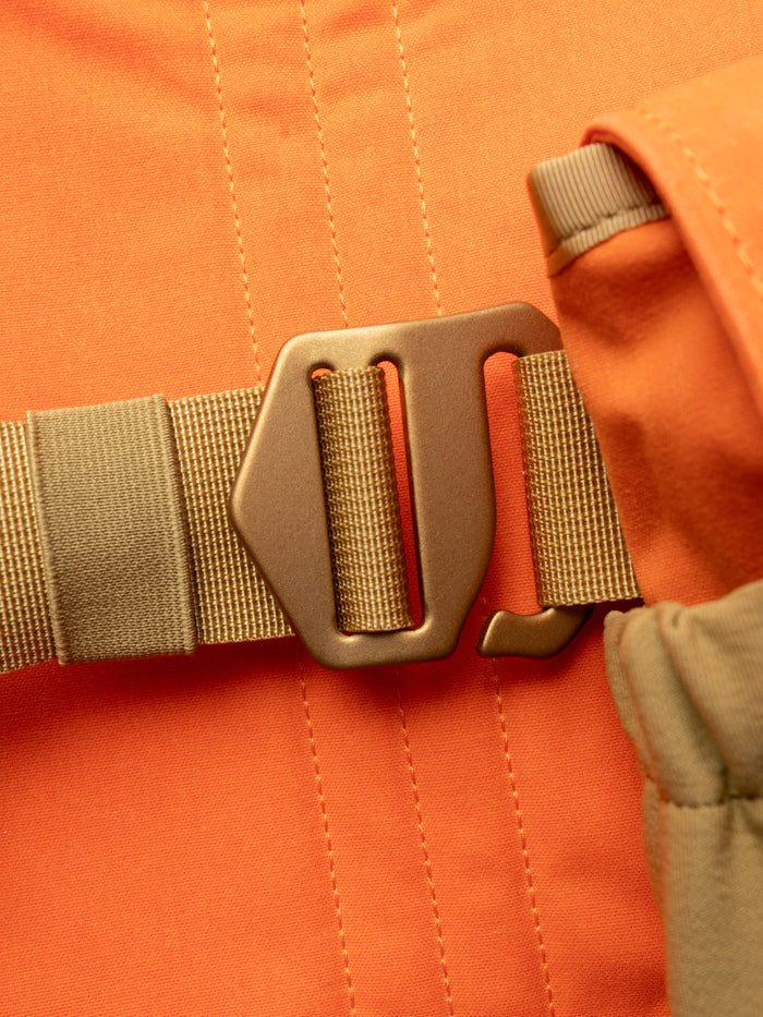 Close-up of a brown plastic buckle fastened to a tan strap on orange fabric, part of the Duck Camp Canvas Upland Strap Vest—durable hunting gear designed for upland pursuits.