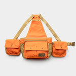 The Duck Camp Canvas Upland Strap Vest is an orange and tan utility vest with three front pockets, tan adjustable straps, and a zippered main compartment, inspired by classic hunting vests and shown against a plain white background.