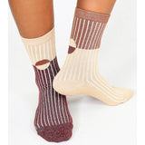 Someone wears Casey Shimmer Ankle Socks by Tailored Union: one sock has maroon and beige vertical stripes, the other beige and brown, both featuring circular accents and ribbed ankles.