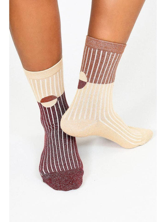 Someone wears Casey Shimmer Ankle Socks by Tailored Union: one sock has maroon and beige vertical stripes, the other beige and brown, both featuring circular accents and ribbed ankles.