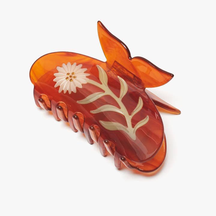 The Winona Irene Chamomile Flower Butterfly Hair Claw in Neutral Tortoise features a translucent amber color with a white flower and green stem design on one side.