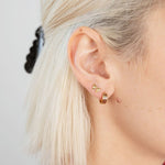 A close-up of a person's ear with short blond hair, wearing two gold earrings: a small butterfly stud and the Checker Huggie Hoops by Larissa Loden, both made from hypoallergenic sterling silver.