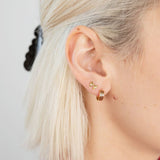 A close-up of a person's ear with short blond hair, wearing two gold earrings: a small butterfly stud and the Checker Huggie Hoops by Larissa Loden, both made from hypoallergenic sterling silver.