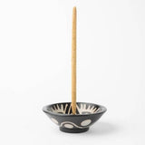 The Chulucanas Ceramic Incense Holder Modelo Clasico by Luna Sundara, handcrafted in Peru, features black ceramic with white abstract designs and holds a burning incense stick upright against a white background.