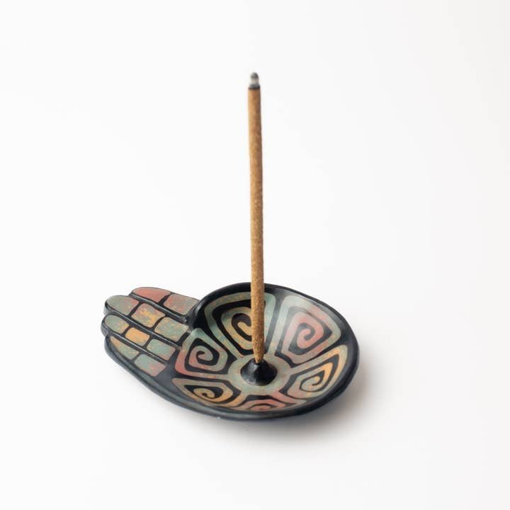 The Chulucanas Ceramic Incense Holder Modelo Mano by Luna Sundara is a hand-shaped, artisan incense holder inspired by traditional pottery, featuring a colorful swirl and holding one stick of burning incense upright.