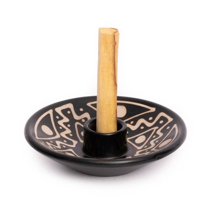 The Chulucanas Ceramics Palo Santo Holder by Luna Sundara is a black ceramic piece with beige geometric patterns, handmade by Peruvian artisans, and holds a central wooden stick upright.