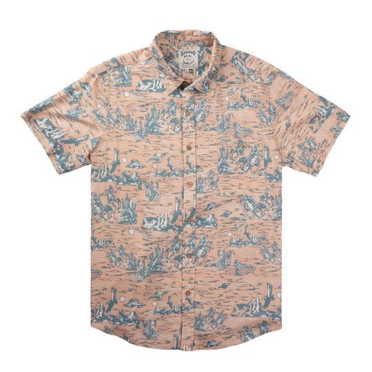 The City Slicker Short Sleeve by Sendero Provisions Co. is a button-up shirt featuring a peach background with a blue scenic print, shown laid flat on a white surface.