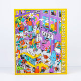 The City Vibes puzzle by Birdie Puzzles features a colorful cityscape by Sarah Matuszewski with people, animals, a taxi, and café. The 1,000-piece box is made from recycled materials and displays “Birdie Puzzles” along the side.
