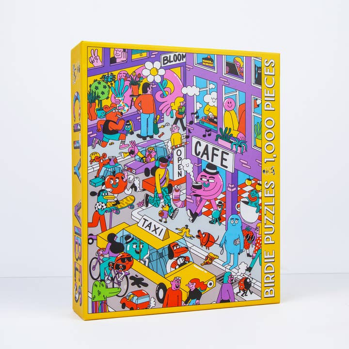 The City Vibes 1,000-piece puzzle by Birdie Puzzles features Sarah Matuszewski’s colorful cartoon city with characters, vehicles, and buildings, packaged in a recycled box.