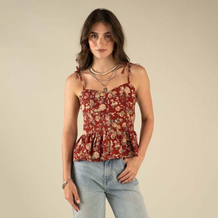 Woman wearing the Clementine Tie Top by Sendero Provisions Co., paired with light blue jeans and layered necklaces, standing against a plain beige background.