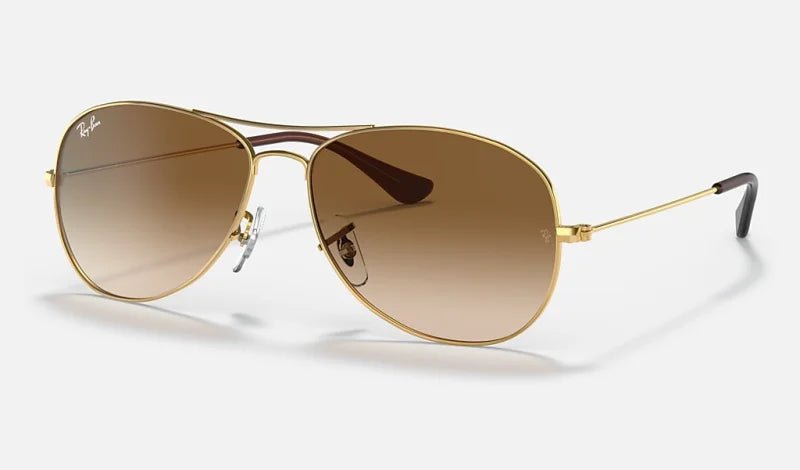 Ray-Ban 3362 Cockpit sunglasses feature thin metal frames, brown gradient lenses, adjustable nose pads, and black plastic arm tips—offering a timeless aviator style.