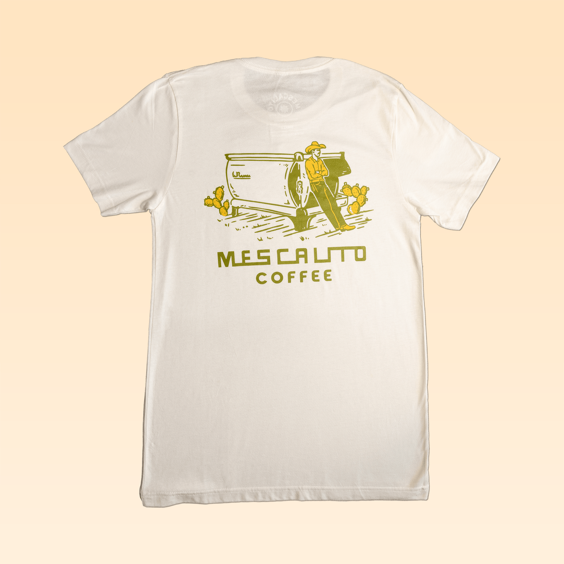 The Coffee Cowboy | Mescalito Coffee shirt by Mescalito Coffee features a white tee with a yellow graphic of a cowboy, coffee machine, cactus, and "Mescalito Coffee" text—perfect for fans of classic cowboy culture.