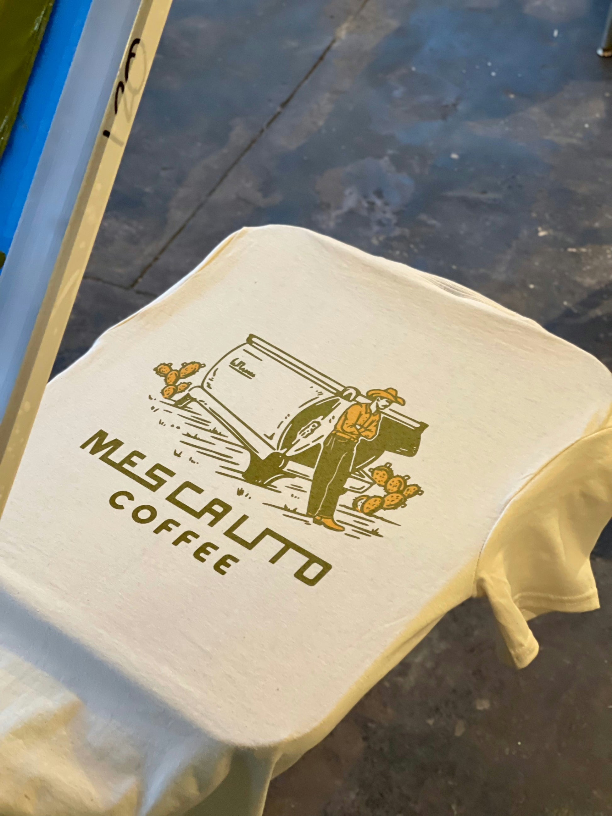 The Coffee Cowboy | Mescalito Coffee shirt by Mescalito Coffee features a printed design of a man, coffee cup, cacti, and the text “Mescalito Coffee”—a tribute to cowboy culture.