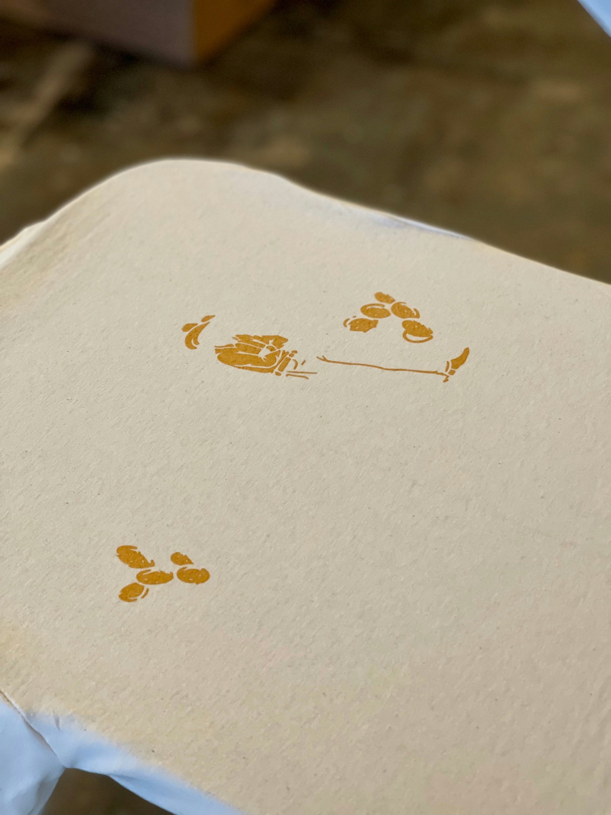 A close-up of beige fabric with yellow-orange abstract footprints, capturing cowboy spirit—perfect for the Coffee Cowboy | Mescalito Coffee shirt by Mescalito Coffee.