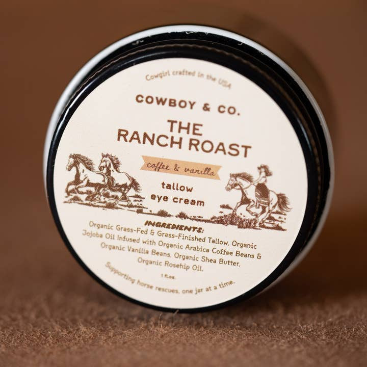 A jar of Cowboy & Co. Coffee/Vanilla Infused Tallow Brightening Eye Cream features a cowboy and horses on the lid and lists organic ingredients.