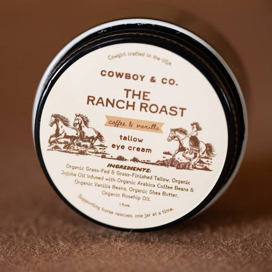A jar of Cowboy & Co. Coffee/Vanilla Infused Tallow Brightening Eye Cream features a cowboy and horses on the lid and lists organic ingredients.