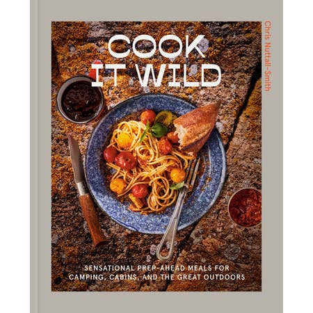 The cover of "Cook it Wild" by Penguin shows a plate of pasta with tomatoes, herbs, and bread on an outdoor surface—ideal inspiration for easy camp cooking and outdoor meals.