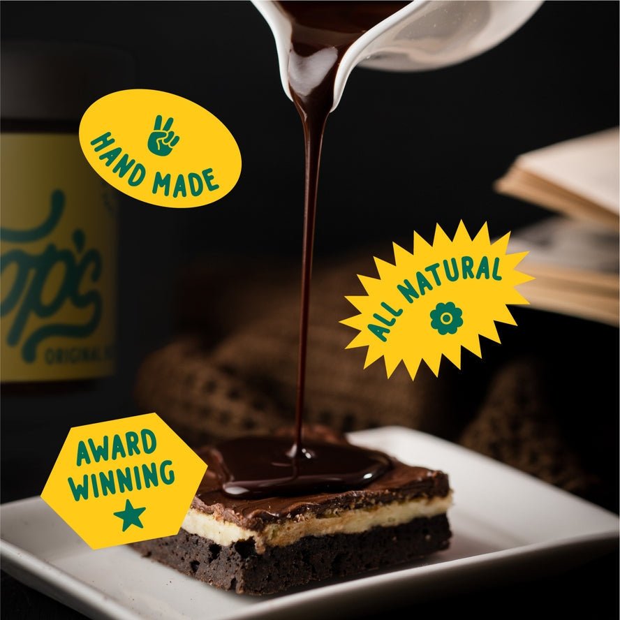 Coop's Original Hot Fudge being poured over a cream-topped brownie, labeled "Hand Made," "All Natural," and "Award Winning"—featuring rich European chocolate sauce by Coop's on a dark background.