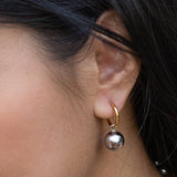 Close-up of a person’s ear wearing Peter and June Cosmo Hoops—18K gold plated hoops with a large, round, stainless steel pendant.