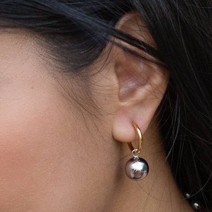 Close-up of a person’s ear wearing Peter and June Cosmo Hoops—18K gold plated hoops with a large, round, stainless steel pendant.