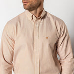 A man stands against a plain background wearing the Duck Head Cotton Oxford Sport Shirt Collins Stripe, a light-colored OCBD with thin vertical stripes and mechanical stretch, his face partially turned to the side.