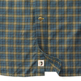 Close-up of the lower part of a Duck Head Cotton Wool Sport Shirt in Orion Blue, yellow, and brown Mercer Plaid, featuring a button and a small bird logo tag near the hem.
