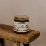 A glass jar of Cowboy & Co. COWBOY Unscented Tallow Moisturizer with a gold lid sits on a rustic wooden stool against a neutral background.