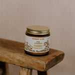 A jar of COWBOY | Unscented Tallow Moisturizer by Cowboy & Co. rests on a rustic wooden stool, its label visible against a neutral background.