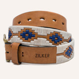 The Cowboy by Zilker Belts features brown Argentine leather with "ZILKER" stamped near the buckle and a white and blue hand-stitched geometric pattern. The belt is displayed coiled in a loop.