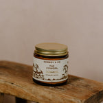 A glass jar labeled "COWGIRL | Vanilla Infused Tallow" by Cowboy & Co. made with grass-fed beef tallow, sits on a rustic wooden stool—ideal for sensitive skin.