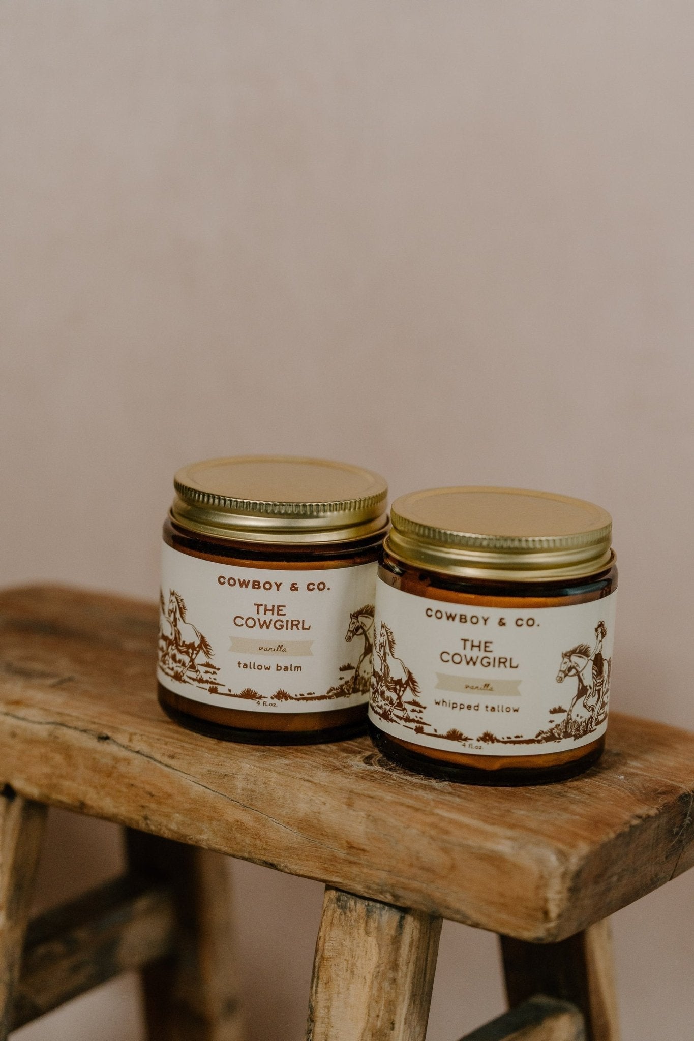 Two jars of Cowboy & Co.'s COWGIRL Vanilla Infused Tallow sit on a rustic wooden stool against a neutral background—ideal for sensitive skin.