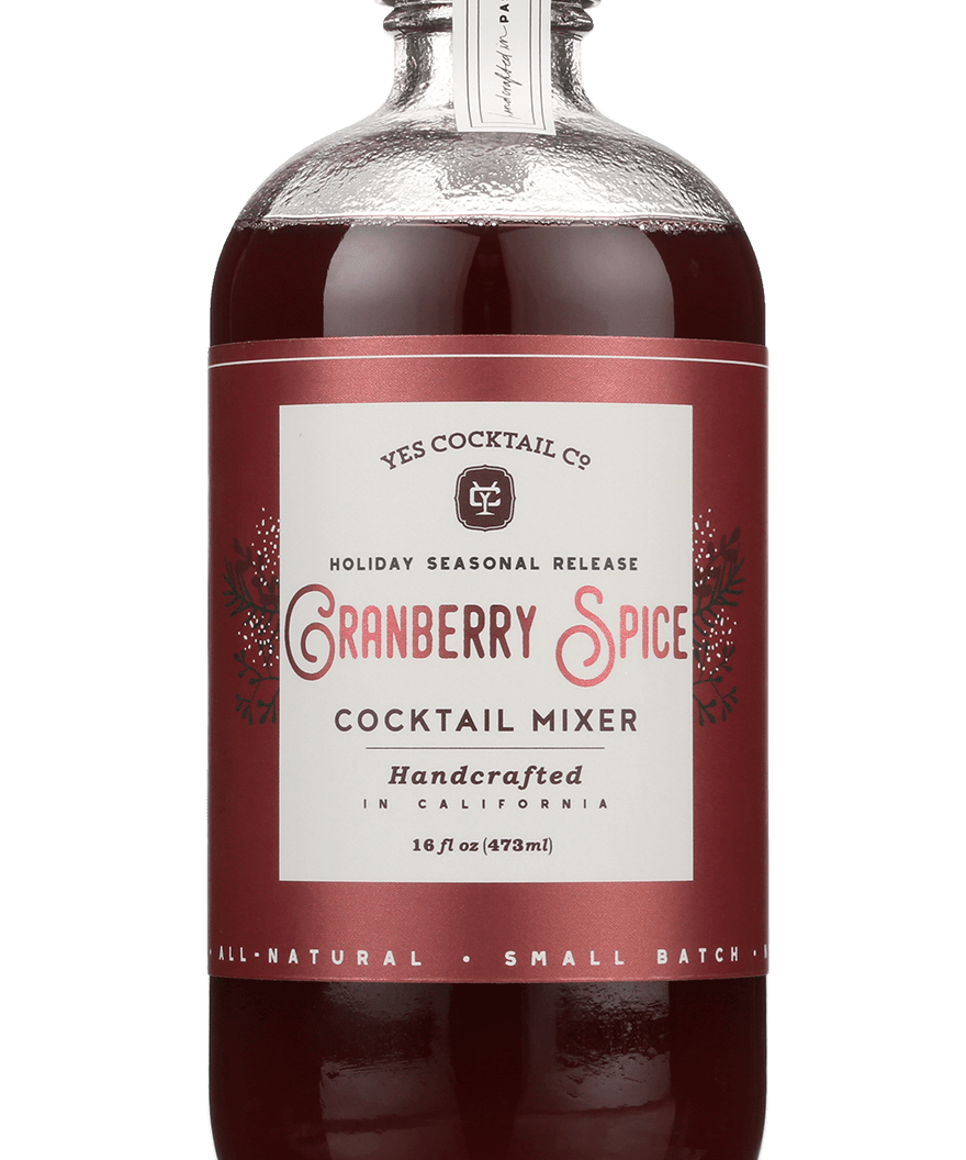 A 16 fl oz (473 ml) glass bottle of red liquid labeled "Cranberry Spice" by Yes Cocktail Co., featuring holiday cocktail mixer seasonal release branding.
