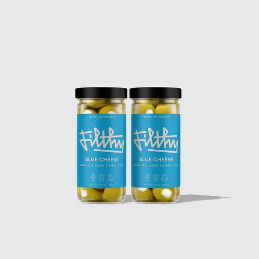 Two jars of Filthy Creamy Blue Cheese Stuffed Olives sit side by side on a plain light gray background—the perfect bold martini garnish, filled with smooth Wisconsin blue cheese.