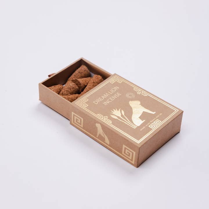 A small open box labeled "Dream Lion Incense" displays several brown, irregular incense cones—each made with sandalwood and rose petals—from the Creative Imagination line by Dream Lion, set against a white background.