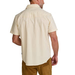 A man shown from the back against a white background wears the Howler Brothers Crosscut Deluxe Snapshirt in Fowl Play, a light beige pearl snap short-sleeve shirt, paired with brown pants.