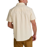 A man shown from the back against a white background wears the Howler Brothers Crosscut Deluxe Snapshirt in Fowl Play, a light beige pearl snap short-sleeve shirt, paired with brown pants.