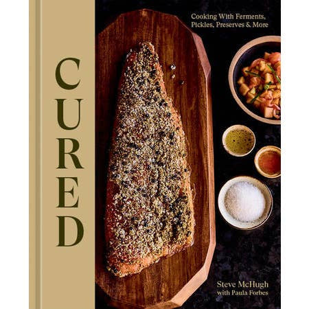 Book cover for "Cured" by Penguin features seasoned cured meat on a wooden board with condiments, highlighting charcuterie and food preservation. Authors: Steve McHugh with Paula Forbes.