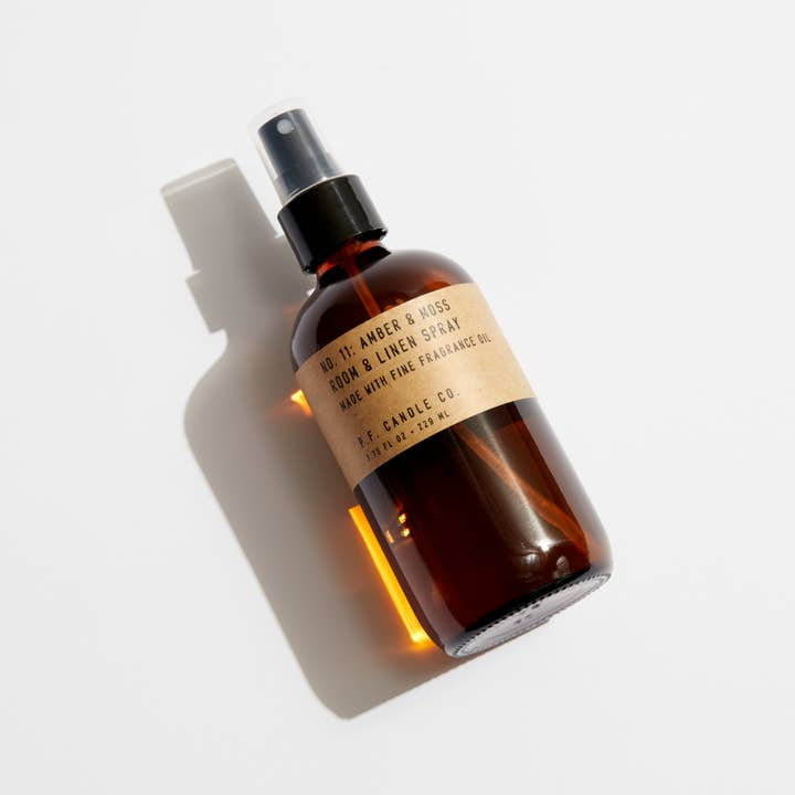 A phthalate-free N0.11 Amber & Moss Room & Linen Spray by P.F. Candle Co., with a black plastic nozzle and amber glass bottle, delivers a clean, refreshing scent for your home.