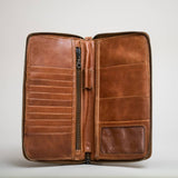 The Stash Passport Wallet in caramel features multiple card slots, a zippered compartment, and a clear ID window, shown open against a plain light background.