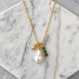 Mesa Blue’s Pearl, Cz Emerald, Star Charm Necklace features 18K gold plating and three pendants—a freshwater pearl, a pavé CZ star charm, and a trio of green gemstone accents—elegantly presented on a white marble surface.