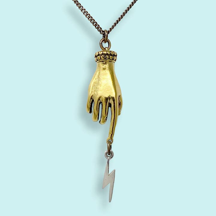 Magician’s Hand Necklace – Aged Brass Chain features an antique gold magician’s hand pendant pointing downward with a sterling silver lightning bolt charm dangling from the index finger.