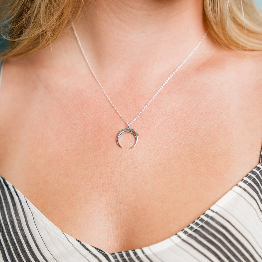 A person wearing the Sterling Silver Crescent Moon Necklace from Ornamental Things—crafted to be nickel free—and a black-and-white striped top with thin straps.