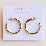 A pair of JaxKelly Everyday Gold Hoop Earrings, hypoallergenic medium hoops, showcased on a white card labeled “JaxKelly Wear Good Vibes.”.
