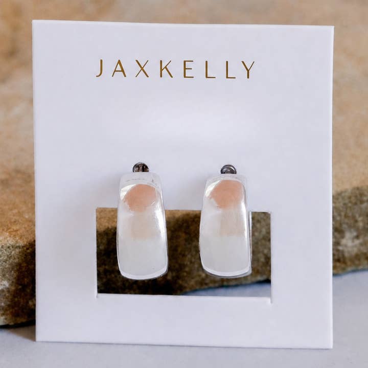 A pair of JaxKelly Silver Hoop - Wide - Earrings, featuring a rectangular design in tarnish-free silver with clear and peach accents, displayed on a white card with the brand name “JaxKelly” in gold lettering. These hypoallergenic earrings are ideal for sensitive ears.