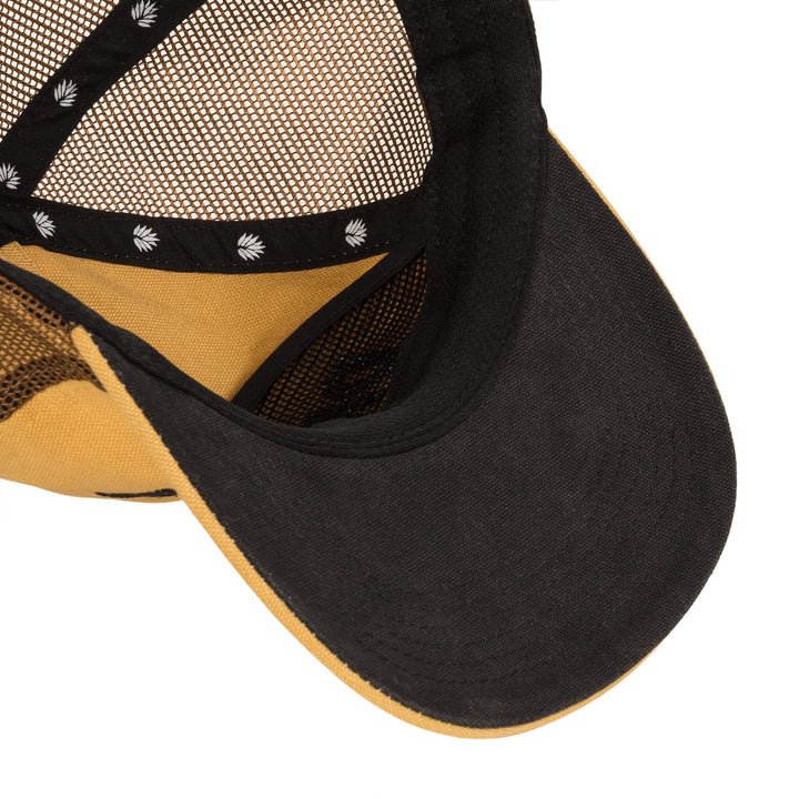 Close-up of the interior of a yellow and black Daggum trucker hat by Sendero Provisions Co., highlighting the brim, mesh paneling, and interior stitching.