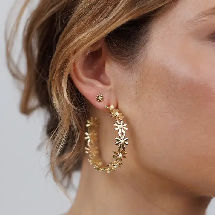 A close-up of a woman's ear showcases the Daisy Chain Hoop earrings by JaxKelly—a large gold floral statement hoop paired with a matching stud, ideal for those seeking tarnish-free daisy flower earrings.