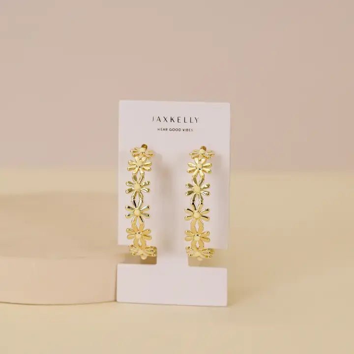 JaxKelly's Daisy Chain Hoop Earrings are displayed on a white card against a beige background. These tarnish-free statement hoops feature daisy flower details, bringing floral elegance to any look.