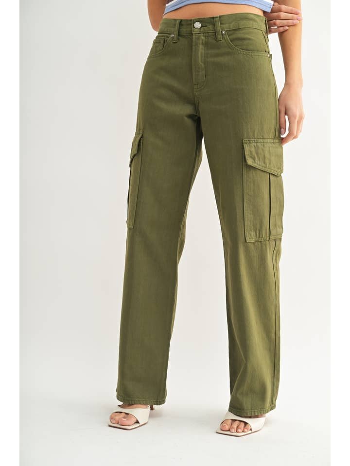 Person wearing JBD's Dark Olive Cargo—high-rise, wide-leg cargo pants with large side pockets—paired with white heeled sandals, standing against a plain background.