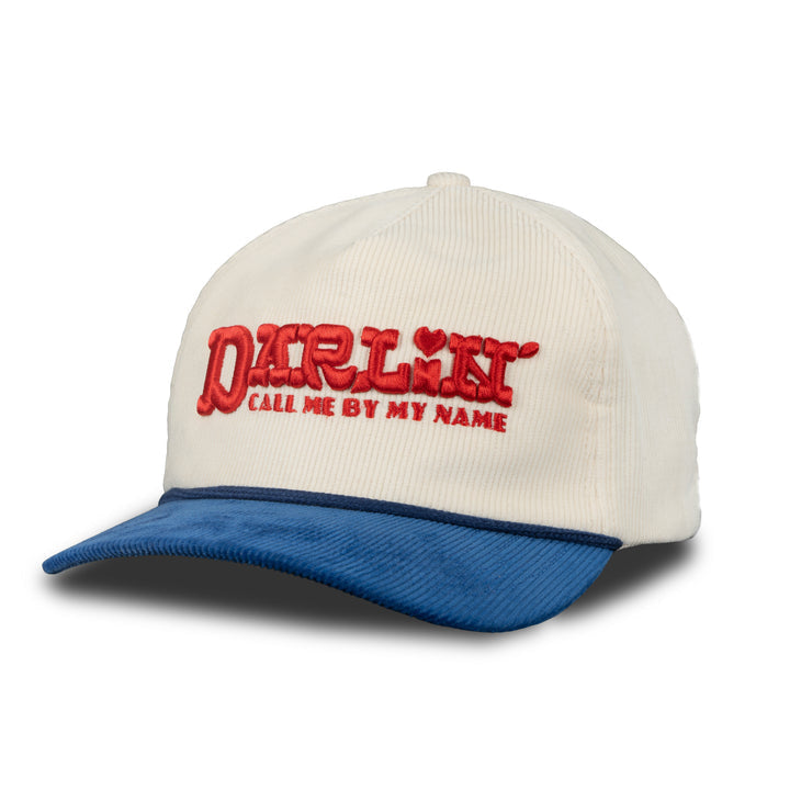The Darlin' Hat by Sendero Provisions Co. is a cream corduroy snapback 5-panel with a blue embroidered visor and red "DARLIN' CALL ME BY MY NAME" text on the front.